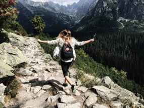 woman walking on rock path at side mountain with arms extended.